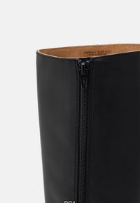 Black leather boot with a smooth texture, featuring a side zipper and a rounded top. Interior shows a light brown lining.