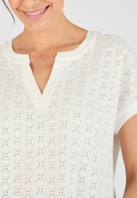 Witte gebreide top met een V-hals, korte mouwen en een gestructureerd open patroon. Beschikt over een ribgebreide halslijn en een licht los zittende pasvorm.
