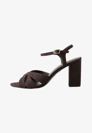 Sandale à talon haut en daim marron foncé avec des brides croisées sur le devant et une bride à la cheville avec boucle dorée.