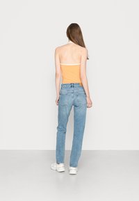 Top halter laranja com bainha branca, combinado com jeans de perna reta azul claro. Modelo a usar ténis brancos, visto de costas.