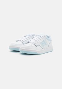 Valged spordijalatsid helesiniste aktsentidega, millel on perforeeritud nahkdisain, ümar varvas ja tekstureeritud kummitald.