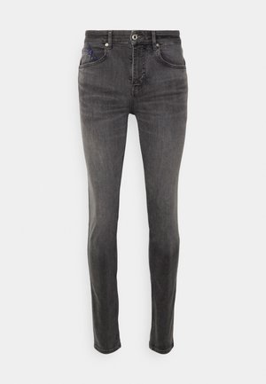 Šedé džíny z denimu s úzkým střihem, vybavené předními kapsami, zipem a jedním modrým detailem na mincovní kapse. Hladká textura.