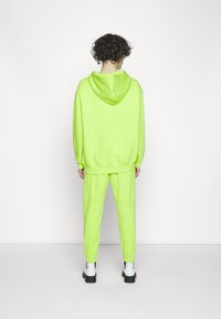 Neon grön hoodie och byxset i mjukt material. Huva bak; joggers har elastiska manschetter. Bärs med svarta och vita ankelskor.