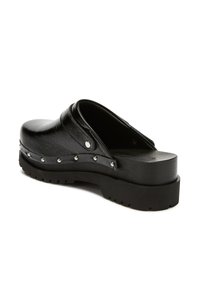 Black leather slip-on clog with thick lug sole and silver studs around the base, angled view showing open back and textured upper.