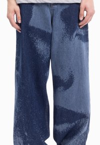 Szerokie spodnie dżinsowe z gradientowym wzorem w ciemnoniebieskich i jaśniejszych odcieniach niebieskiego, wykonane z bawełny o przetartej fakturze.