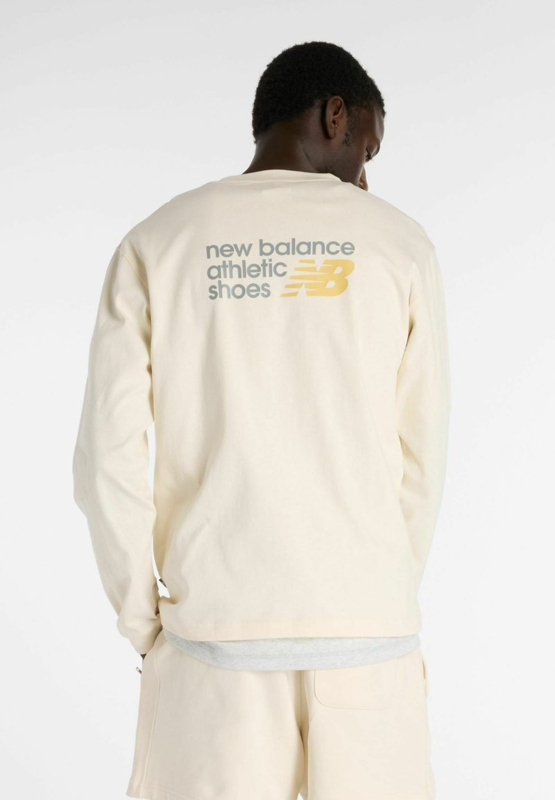 Crème lange mouw shirt met een ontspannen pasvorm, voorzien van ‘new balance sportschoenen’ in grijs en geel gedrukt op de achterkant.