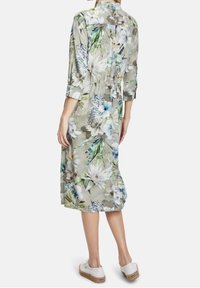 Blommönstrad klänning i ljusgrått tyg, med trekvartsärmar, midjesnöre och knälång längd, i kombination med vita skor.