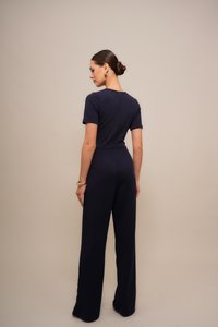 Marineblauwe jumpsuit met korte mouwen, een getailleerde taille en wijde pijpen. Voorzien van een ritssluiting aan de achterkant en een soepele stofstructuur. Minimalistisch ontwerp.