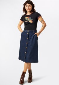 T-shirt noire avec un graphique "King Louie", associée à une jupe en jean foncé taille haute, longueur genoux, avec une fermeture à boutons sur le devant et des poches.