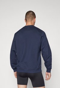 Sudadera azul marino con cuello redondo y mangas largas, que presenta una textura suave y puños y dobladillo acanalados. Vista posterior mostrada.