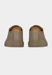 Ζευγάρι μπεζ σουέντ αθλητικά παπούτσια χαμηλού ύψους, ορατά από πίσω, με υφασμένες λωρίδες στη φτέρνα και λαστιχένιες σόλες σε λευκό φόντο.