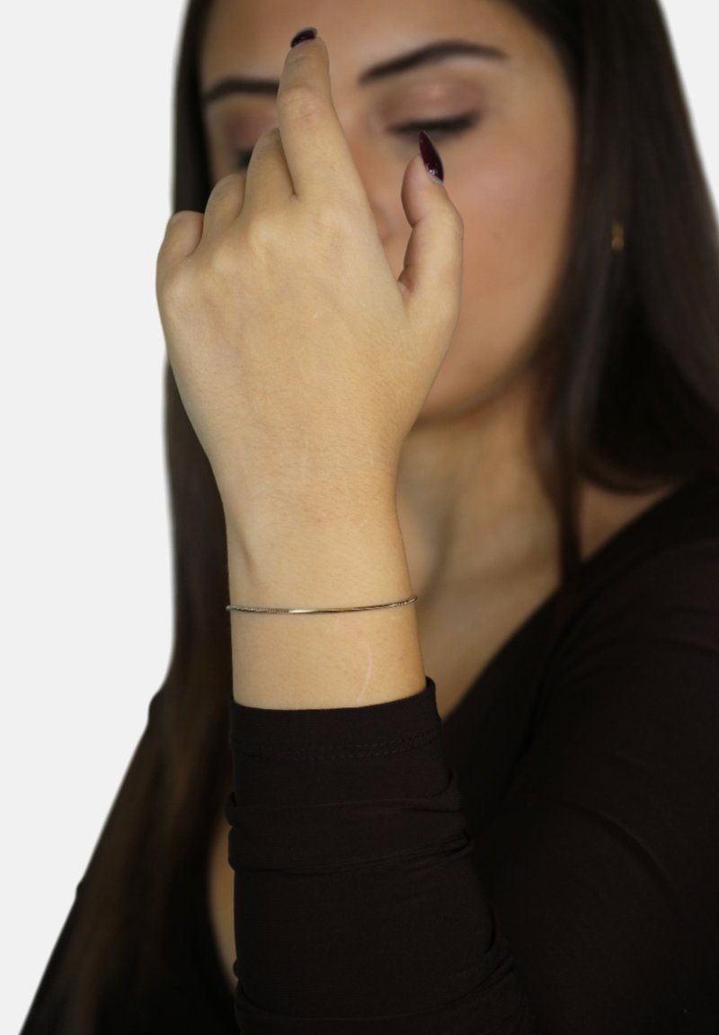 Bracciale in metallo argentato su una mano, con una finitura liscia e lucidata e un design flessibile, indossato con una maglietta a maniche lunghe scura.