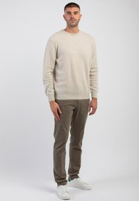Maglione beige a costine con scollo rotondo, abbinato a pantaloni slim-fit marrone chiaro e sneakers bianche con dettagli verdi.