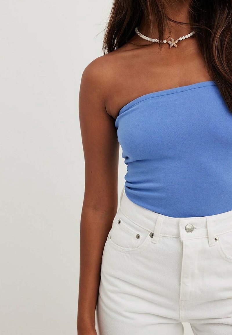 Blå strapless topp, figursydd design, tillverkad av mjukt tyg; kombinerad med högmidjade vita denimshorts med silverdetaljer.