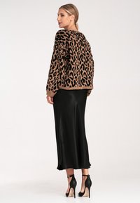 Leopardenmuster Strickpullover in Braun und Schwarz, kombiniert mit einem schwarzen Satin-Maxikleid und schwarzen Ankle-Strap-Pumps.