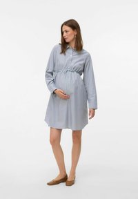 Abbigliamento premaman in stile chemisier a righe in azzurro chiaro e bianco, con vita aderente e fiocco, maniche lunghe e gonna morbida. Realizzato in morbido cotone.