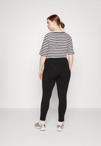 Leggings pretos com um design ajustado, combinados com uma blusa de manga curta listrada em azul marinho e rosa. Ténis com detalhes em prata.