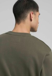 Felpa verde oliva con design semplice, scollo girocollo a coste e tessuto morbido. Vista posteriore e spalle con dettagli minimi.