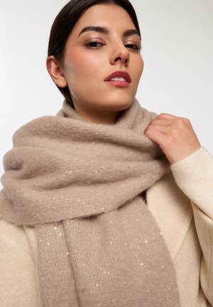 Sciarpa beige realizzata in un tessuto morbido, con delicate decorazioni, avvolta attorno al collo. Indossata con un maglione color crema.