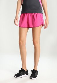 Pantalones cortos deportivos rosas de corte holgado, diseñados con una cintura elástica. Combinados con zapatillas de correr negras con un upper texturizado.