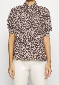 Braune Bluse mit floralen Mustern, Rüschensaum am hohen Kragen und kurzen Ärmeln. Verfügt über ein texturiertes Druckbild mit cremefarbenen und gelben Blumenmustern.