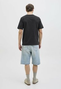 Camiseta de algodón negra con mangas cortas, combinada con pantalones cortos de mezclilla azul claro. El calzado son unos zapatos slip-on grises con suela beige y calcetines claros.