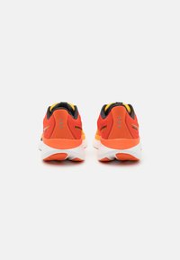 Chaussures de sport rouges et orange avec des accents noirs, semelle blanche rembourrée, matériau texturé et une marque distincte sur le talon.