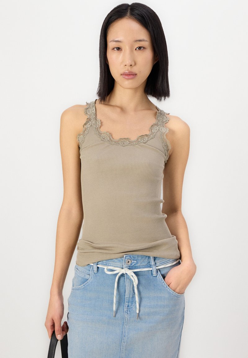 Beige geripptes Tanktop mit gewelltem Spitzenbesatz am Halsauschnitt und den Armöffnungen, kombiniert mit einem hellblauen Denimrock mit Kordelzugbund.