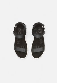 Svart sandal med justerbara remmar vid foten och ankeln. Mjukt mockamaterial, minimalistisk design, vit sula och präglad "Kvinnor" på innersulan.