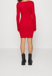 Abito rosso aderente a coste con maniche lunghe, tessuto liscio, lunghezza sopra il ginocchio, abbinato a stivali neri alla caviglia, design minimalista.