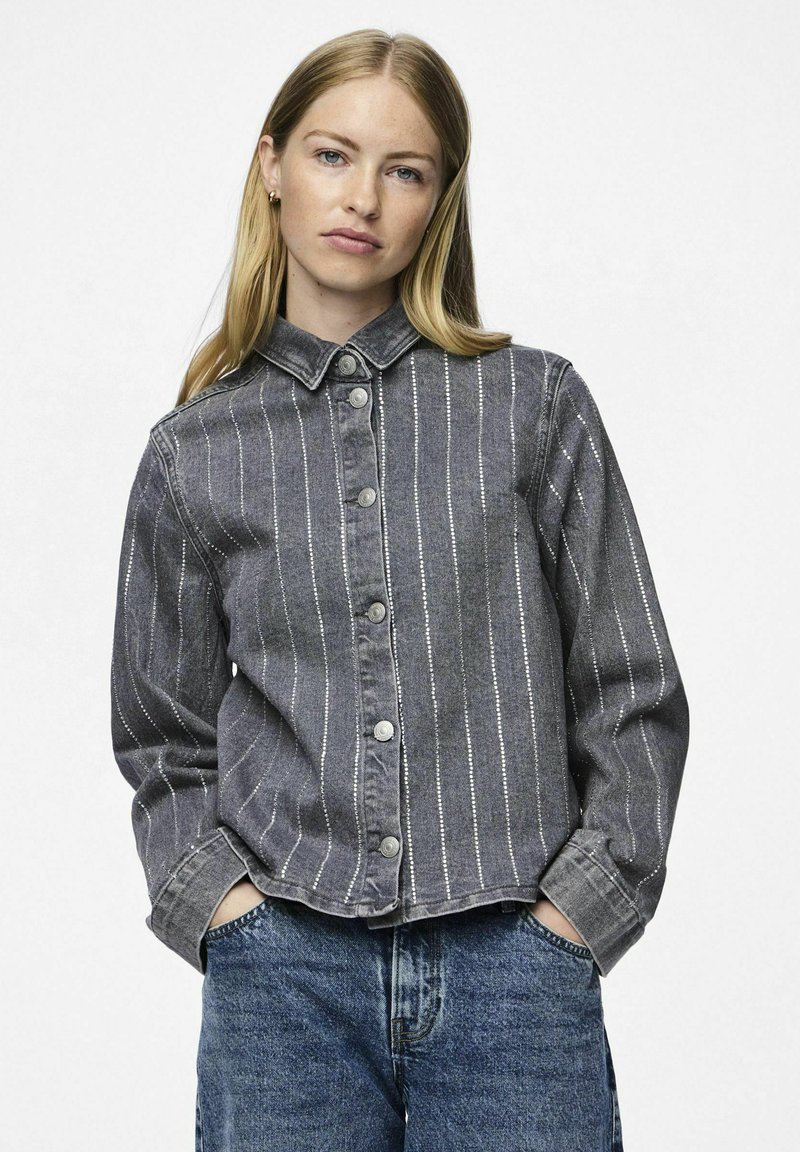 Giacca di jeans grigia con righe verticali bianche, chiusura con bottoni, colletto a punta e maniche lunghe. Indossata con jeans di denim blu.