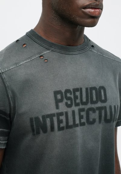 Graues T-Shirt mit abgenutzten Schulterdetails, rundem Halsausschnitt und fettem schwarzen Text mit der Aufschrift "PSEUDO INTELLECTUM." Weiche Textur.