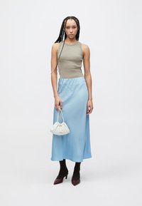 Sleeveless olive top paired with a light blue satin skirt. Accessorized with a white gathered handbag and burgundy pointed-toe heels.
