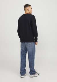 Sudadera negra con cuello redondo, combinada con unos vaqueros de mezclilla azul holgados. Zapatillas deportivas con un patrón multicolor completan el look.