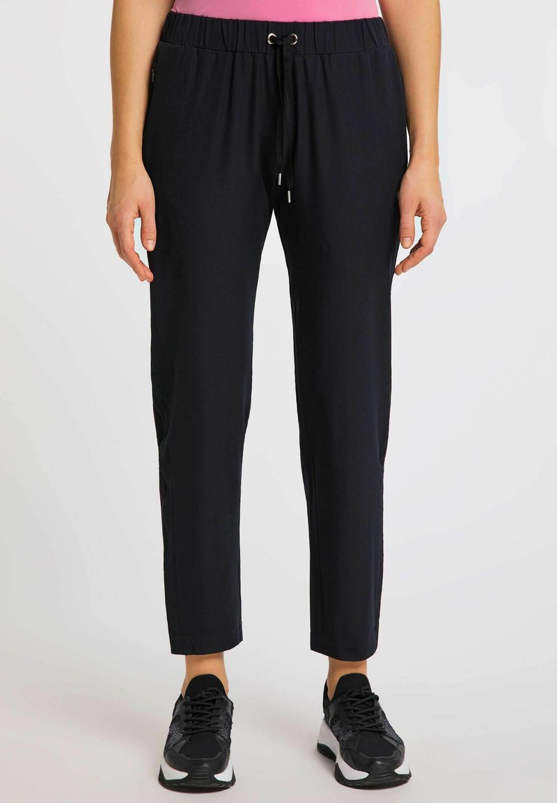 Czarne, lekkie spodnie dresowe z elastycznym paskiem w talii i sznurkiem. Zwężane nogawki i gładka tekstura. W komplecie z czarnymi butami sportowymi.