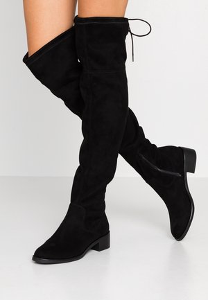 Bottes noires en suède montantes jusqu'au genou, avec une surface texturée, un talon plat et un détail en dentelle en haut, présentant un design élégant.