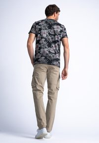 Camisa negra de flores de manga corta para hombres con estampados en rosa y blanco, combinada con pantalones cargo color caqui. Zapatillas blancas completan el conjunto.