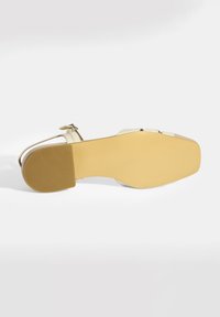 Beige open-toe sandaal met een gestructureerde gele zool, voorzien van twee banden en een gesp, gladde afwerking en een brede vierkante neus.