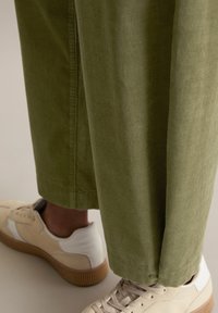 Khaki kordurojowe spodnie z szerokimi nogawkami i lekką tekstur�ą, w połączeniu z beżowymi sneakerami z brązową podeszwą i białymi akcentami.