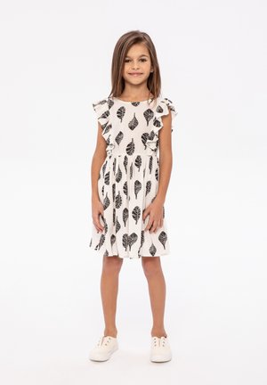 Robe blanche avec des motifs de feuilles noirs, manches à volants et taille élastique, associée à des baskets blanches. Texture de tissu lisse.