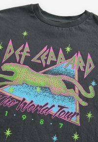 Schwarzes Baumwoll-T-Shirt mit einem lebhaften grafischen Design eines springenden Leoparden in Grün und Pink, akzentuiert durch geometrische Formen und Sterne.