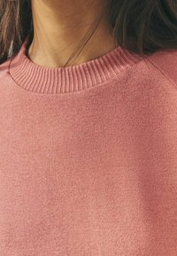 Pull rose avec un col ras du cou côtelé, fabriqué en tissu doux avec une texture lisse et des détails de couture minimes.