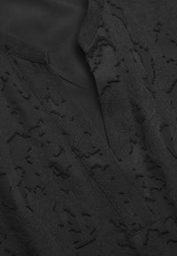 Schwarzes Kleid mit strukturierten Blumenmustern, tiefem V-Ausschnitt und glattem Stoffbasis, das geschichtete und elegante Designelemente kombiniert.