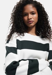 Biały sweter z wyraźnymi poziomymi czarnymi paskami, z okrągłym dekoltem i luźnymi rękawami, wykonany z miękkiego materiału o przyjemnej w dotyku fakturze.