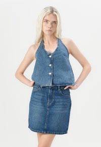 Sötétkék mosású farmer pántos felső, gombos elejével és rövidített fazonja, amely egy azonos anyagú farmer szoknyával van párosítva.