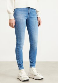Ljusblå skinny jeans av denim, med en slät yta och en lätt urblekning. Kombineras med vita högskor.
