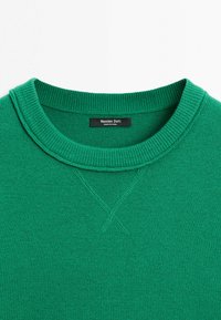 Grøn strikket crewneck-trøje med ribbet krave og dekorativt syet "X" under kraven, Massimo Dutti-mærke indeni halsudskæringen.