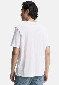Camiseta de algodón blanca con cuello redondo, mangas cortas y un corte relajado, mostrada desde la parte posterior contra un fondo blanco liso.