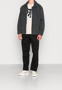 Gray striped jacket with two front pockets, beige graphic t-shirt, black pants, and cream sneakers featuring floral embroidery.