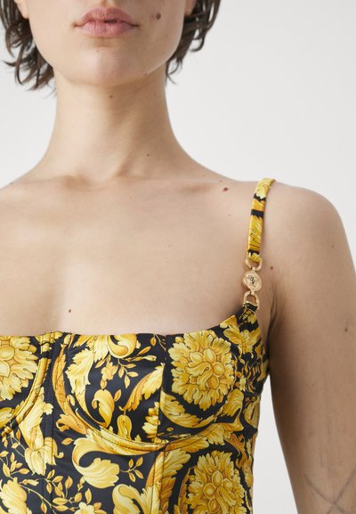 Μαύρη ύφασμα μπλούζα με κίτρινο λουλουδάτο σχέδιο, με δομημένο σχέδιο, λεπτές τιράντες και χρυσές λεπτομέρειες στη τιράντα.